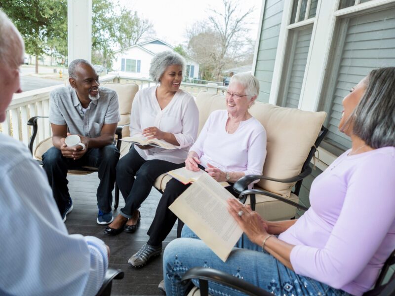 A group of diverse retired senior adults enjoy participating in a book club in an active retirement community. They are sharing their opinions of the book.